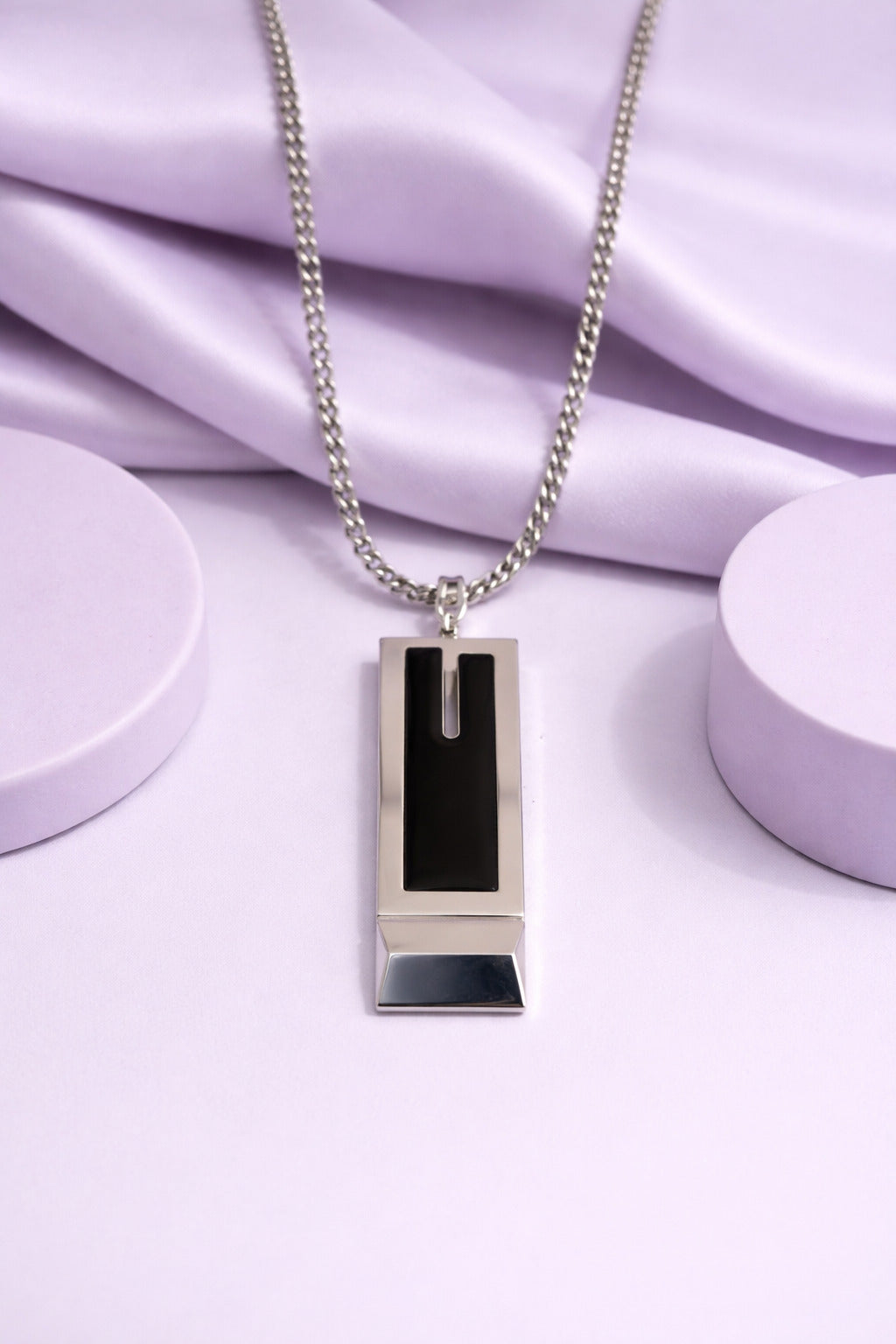 Silver necklace with a rectangular pendant on a light purple fabric background