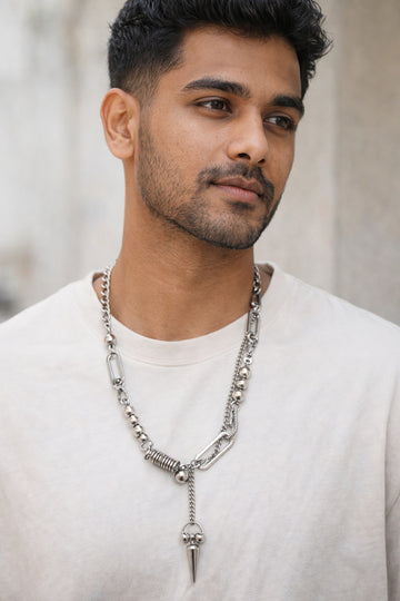 Man wearing a silver chain necklace with a pointed pendant against a neutral background