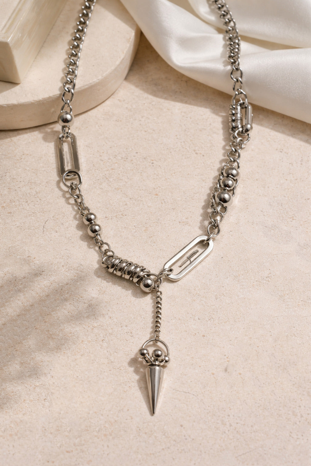 Silver chain necklace with a spike pendant on a beige surface