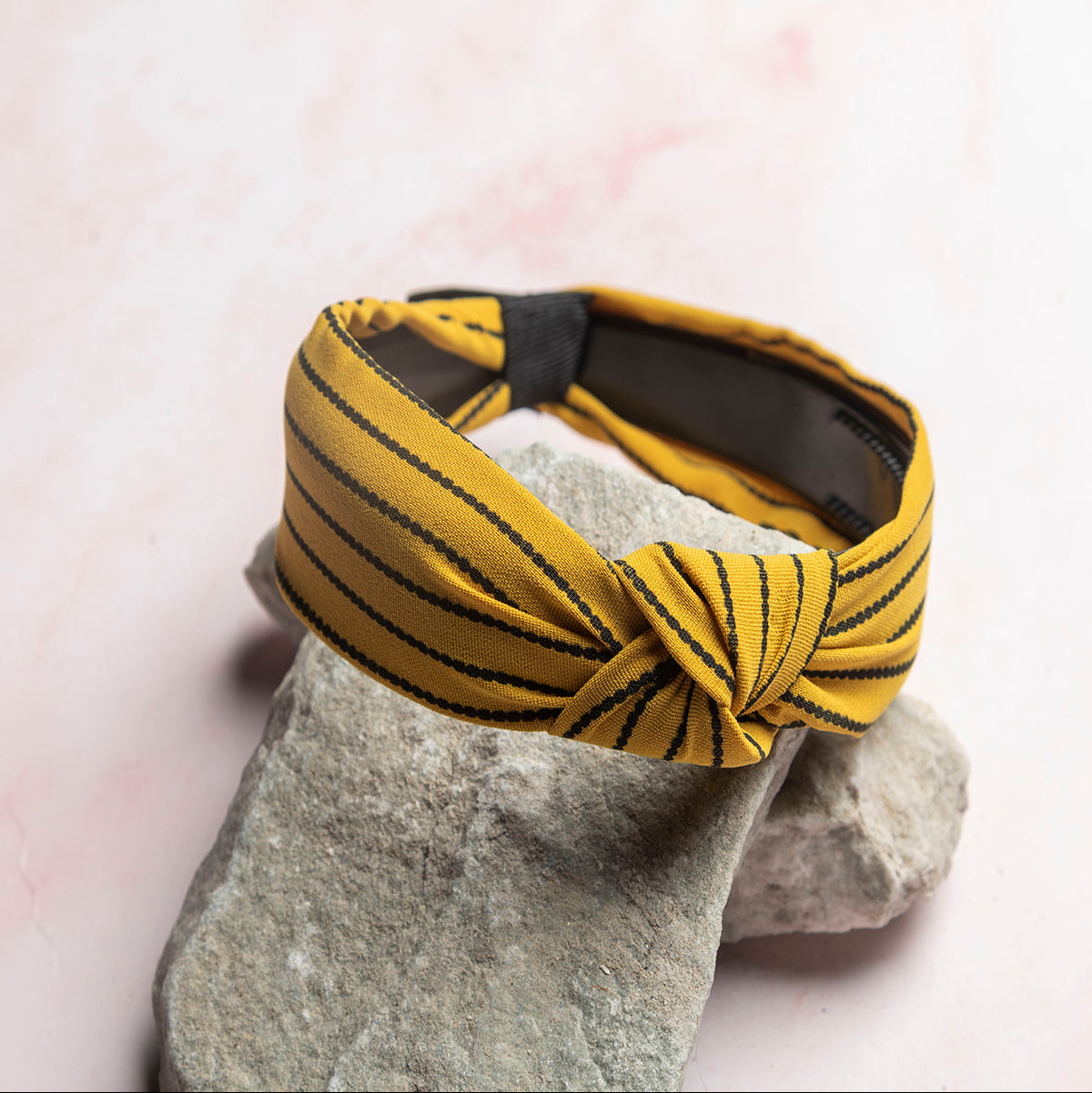 Yellow striped headband on a textured stone surface with a pink background
