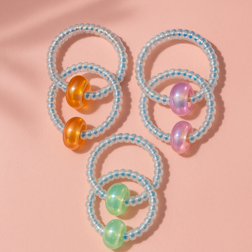 Three beaded hair ties with colorful beads on a pink background