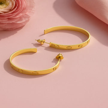 Gold hoop earrings on a pink background with a pink flower.