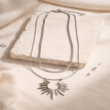 Silver necklace with a sunflower pendant on a beige surface