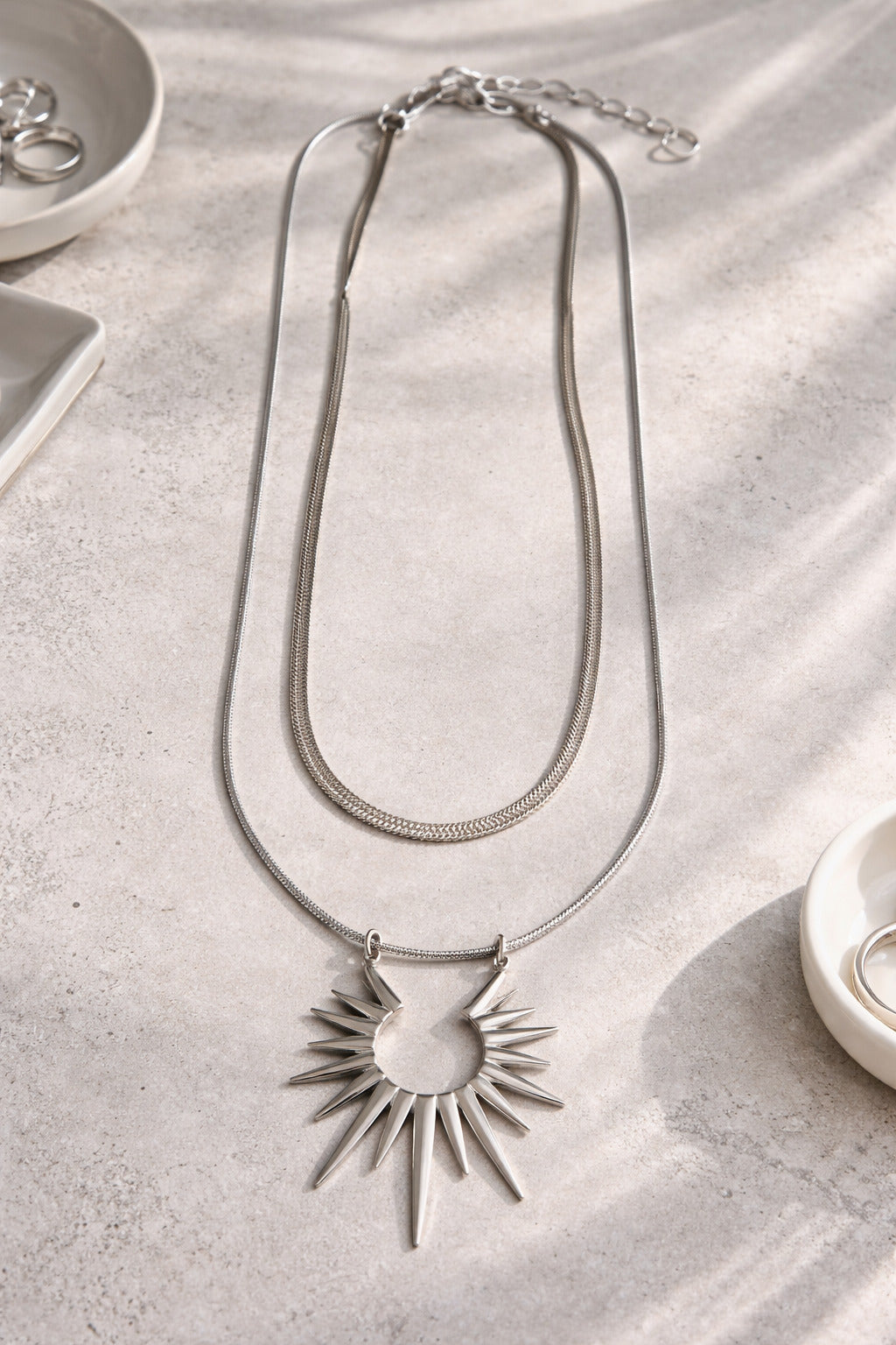 Silver necklace with sun pendant on a textured surface