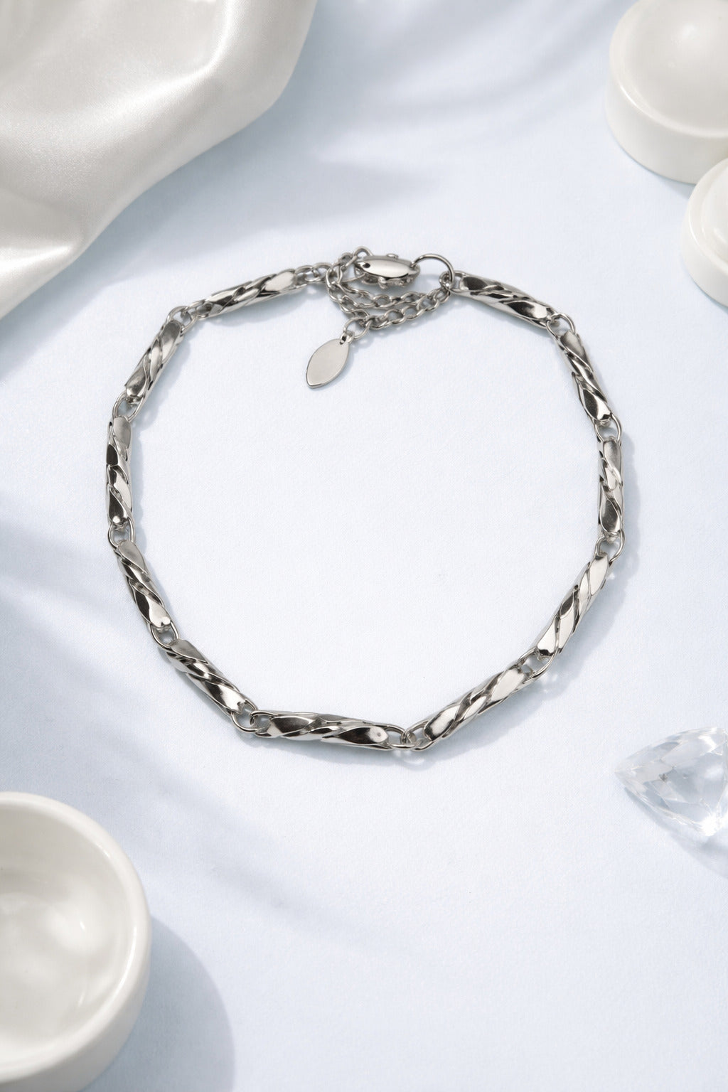 Silver chain necklace on a light blue surface with white ceramic bowls.