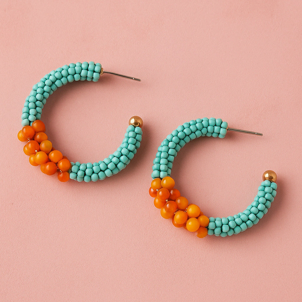 Turquoise and orange beaded hoop earrings on a pink background