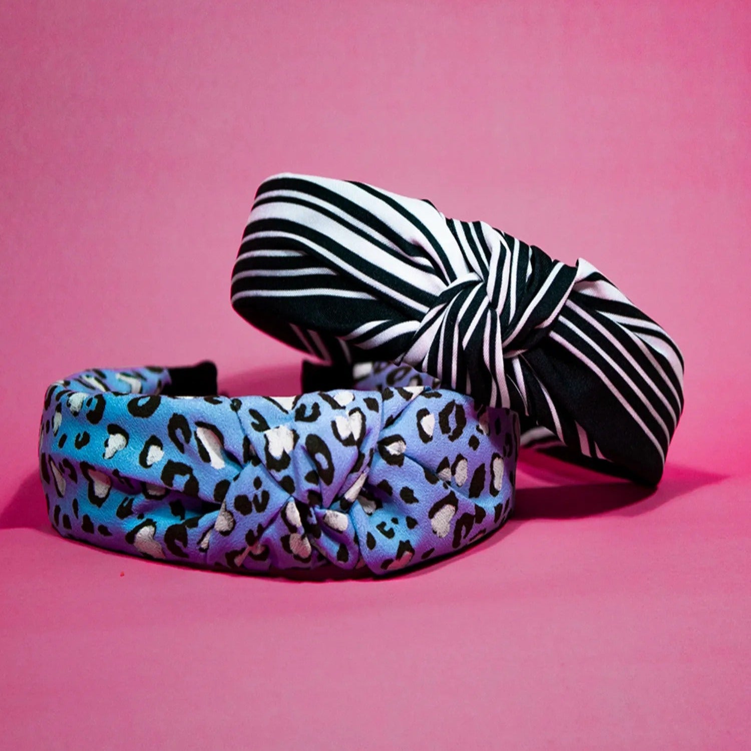 Two hairbands, one with a multicolored animal print and the other with a black and white striped pattern, displayed against a pink background.