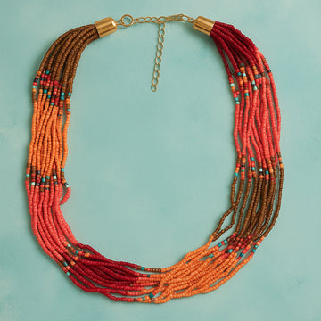 Multistrand beaded necklace with red and orange beads on a light blue background