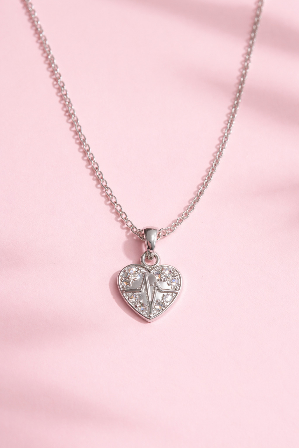 Silver heart-shaped pendant necklace on a pink background