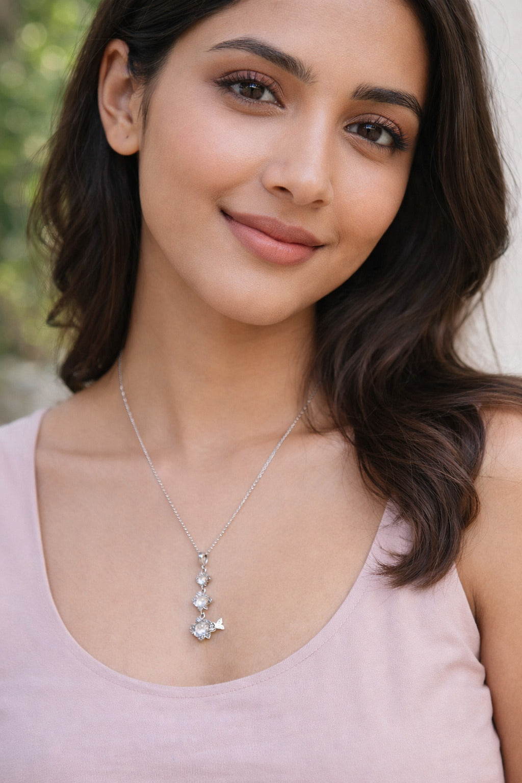 Woman wearing a silver necklace with a pendant against a blurred natural background
