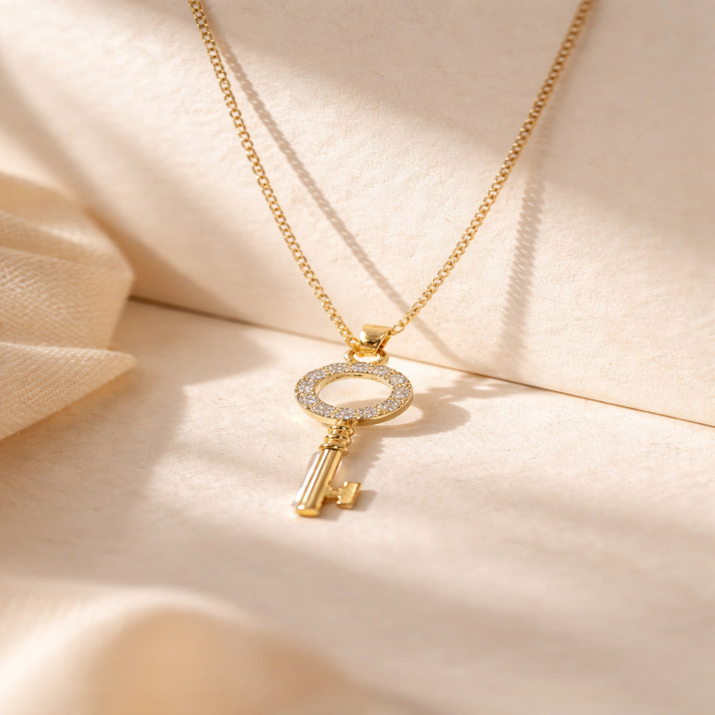 Gold key-shaped pendant necklace on a beige fabric background