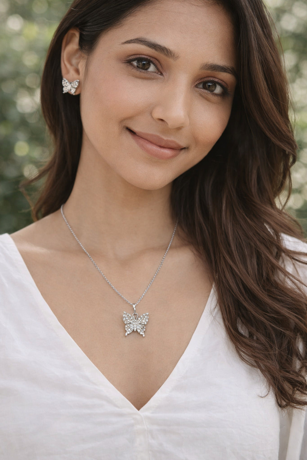 Woman wearing a butterfly necklace and earrings with a blurred natural background
