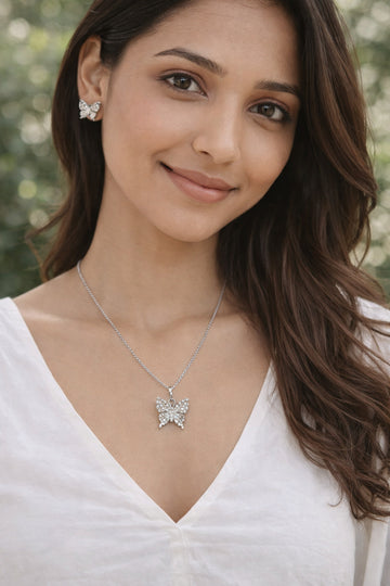 Woman wearing a butterfly necklace and earrings with a blurred natural background