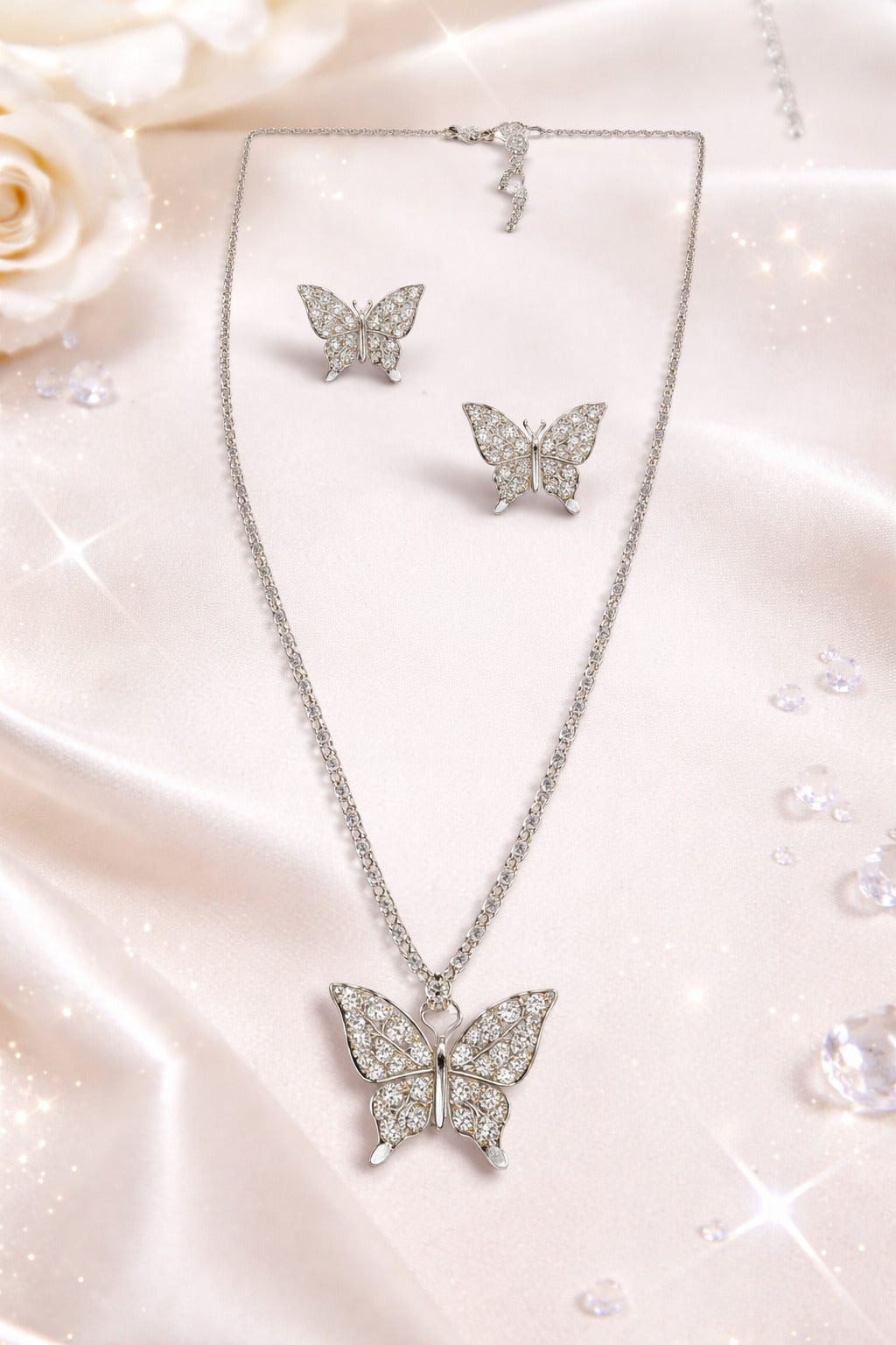 Butterfly necklace and earrings set on a soft pink fabric background