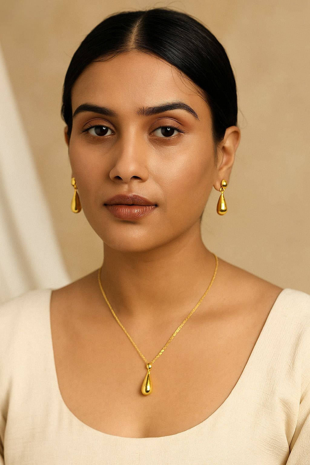 Woman wearing gold jewelry including earrings and a necklace against a beige background