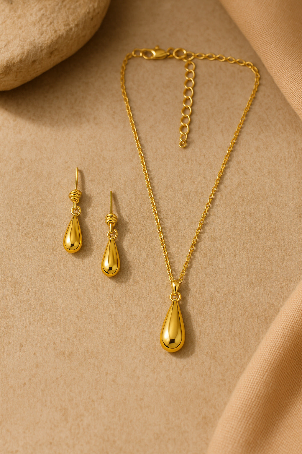 Gold necklace and earrings set on a beige fabric background