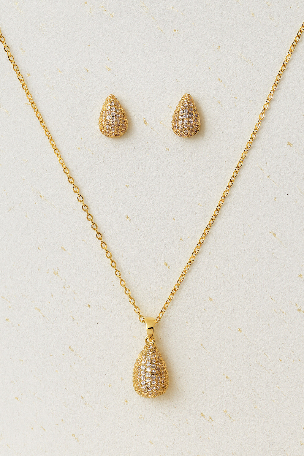 Gold necklace and earrings set on a light beige background