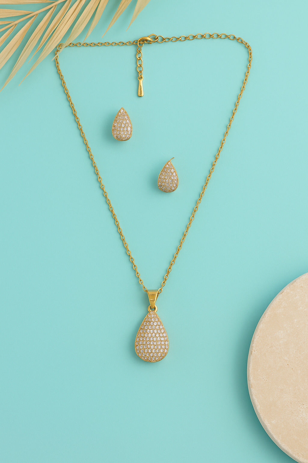 Gold teardrop necklace and earrings on a turquoise background