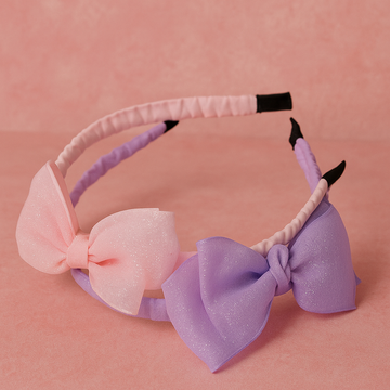 Two headbands with pink and purple bows on a pink background