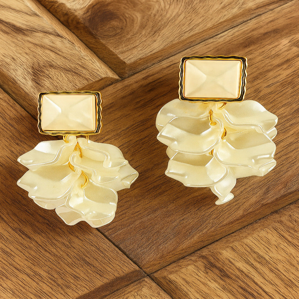 Pair of earrings with beige stones and gold accents on a wooden surface