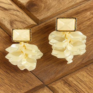 Pair of earrings with beige stones and gold accents on a wooden surface
