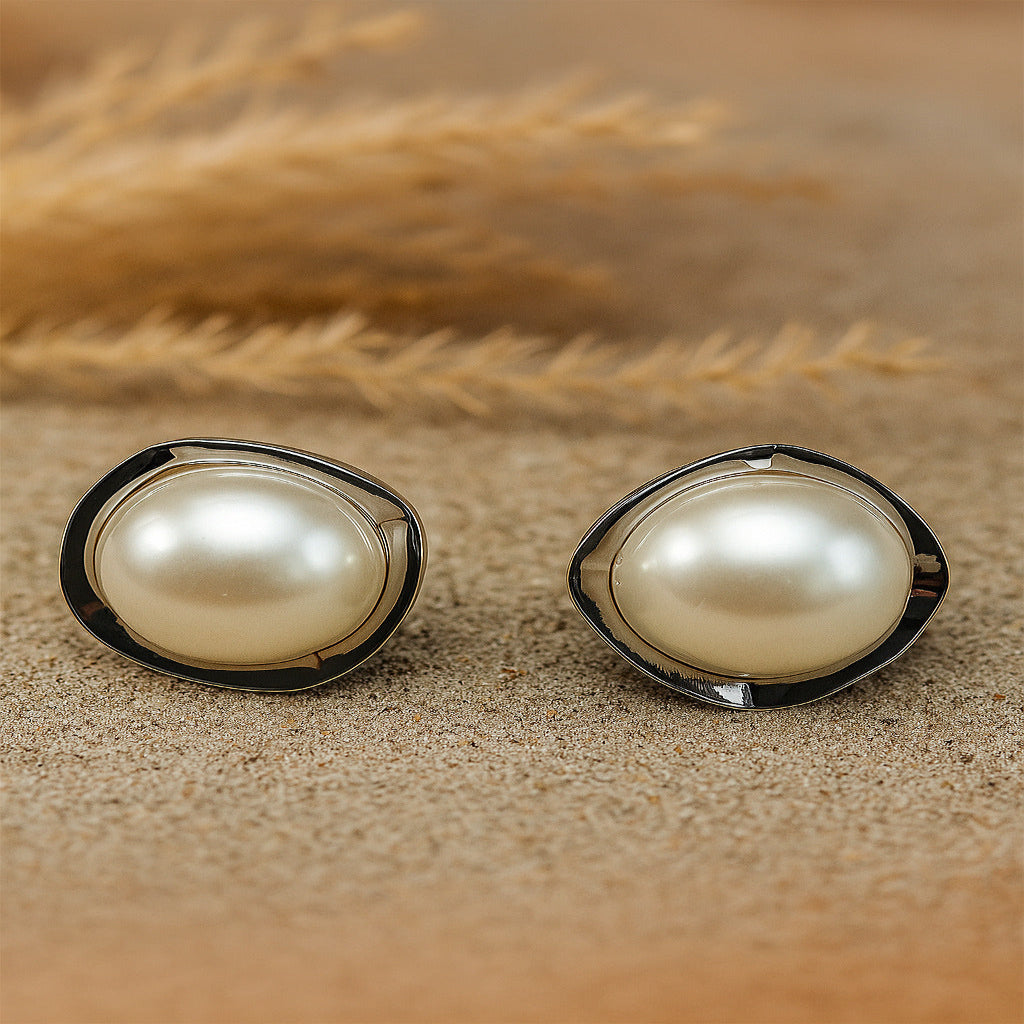 Pair of pearl earrings on a sandy surface with dried grasses in the background