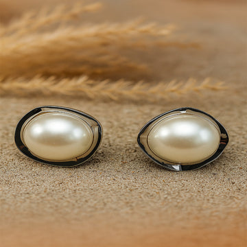 Pair of pearl earrings on a sandy surface with dried grasses in the background