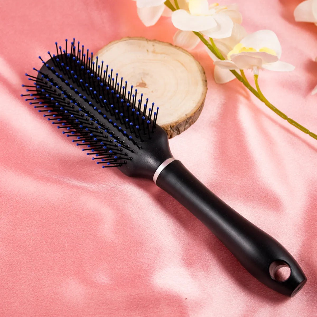 A black plastic hair comb with blue bristles, positioned on a pink surface with a floral design in the background.