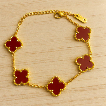 Gold bracelet with red clover-shaped charms on a wooden surface