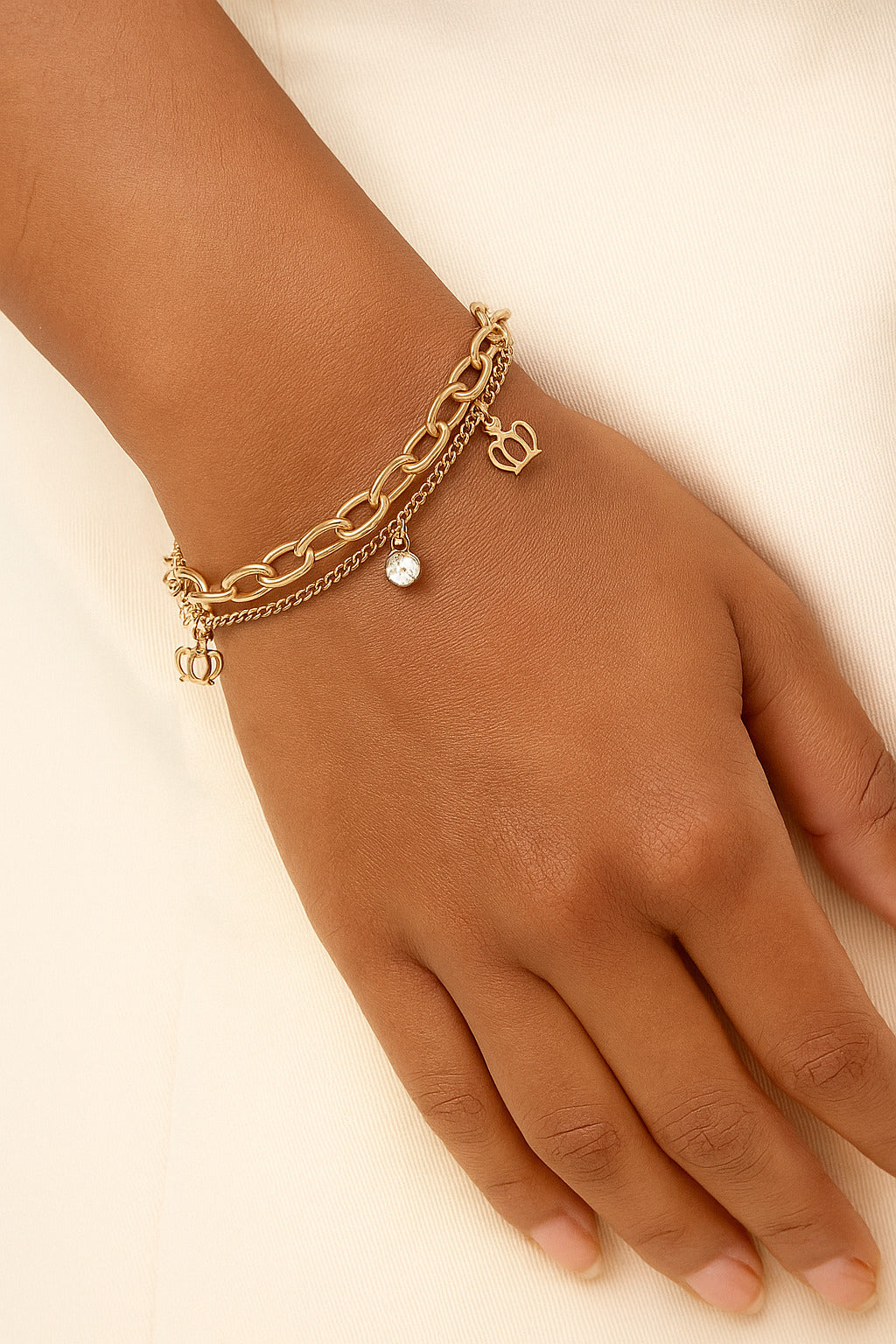 Gold chain bracelet with heart charm on a wrist against a beige background