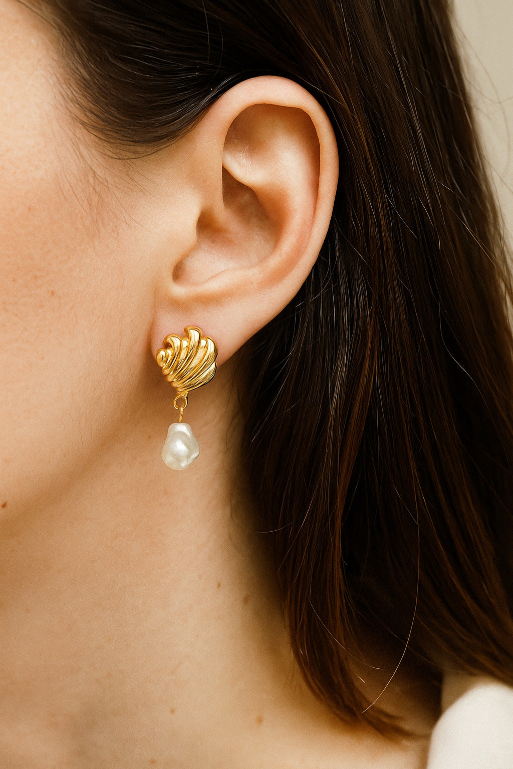 Close-up of a person wearing a gold earring with a pearl drop.