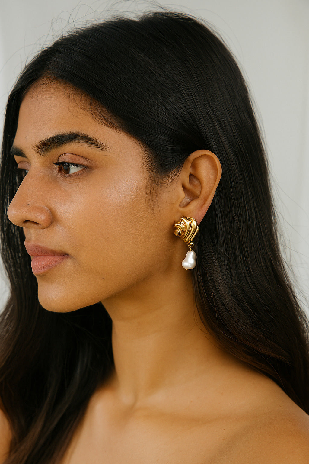 Woman wearing gold earrings with a pearl accent against a neutral background