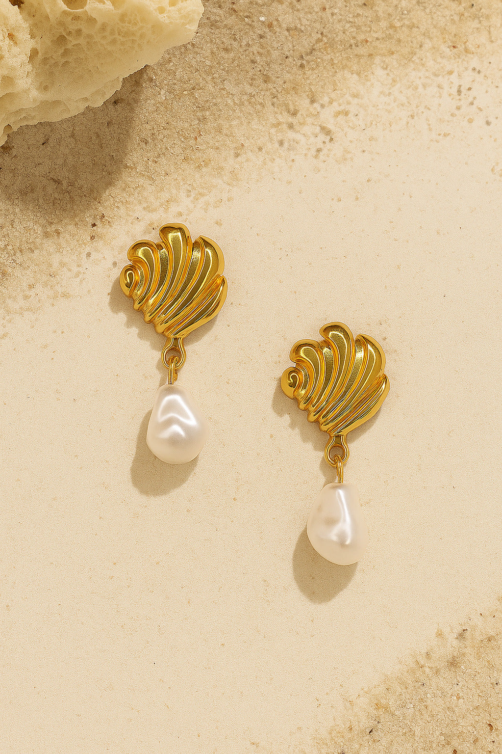 Gold earrings with pearl drops on a beige background