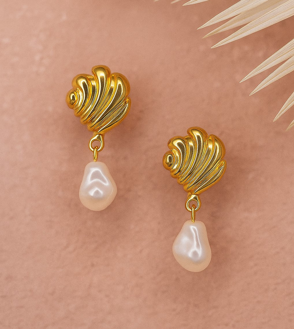Gold shell-shaped earrings with pearl drops on a beige background