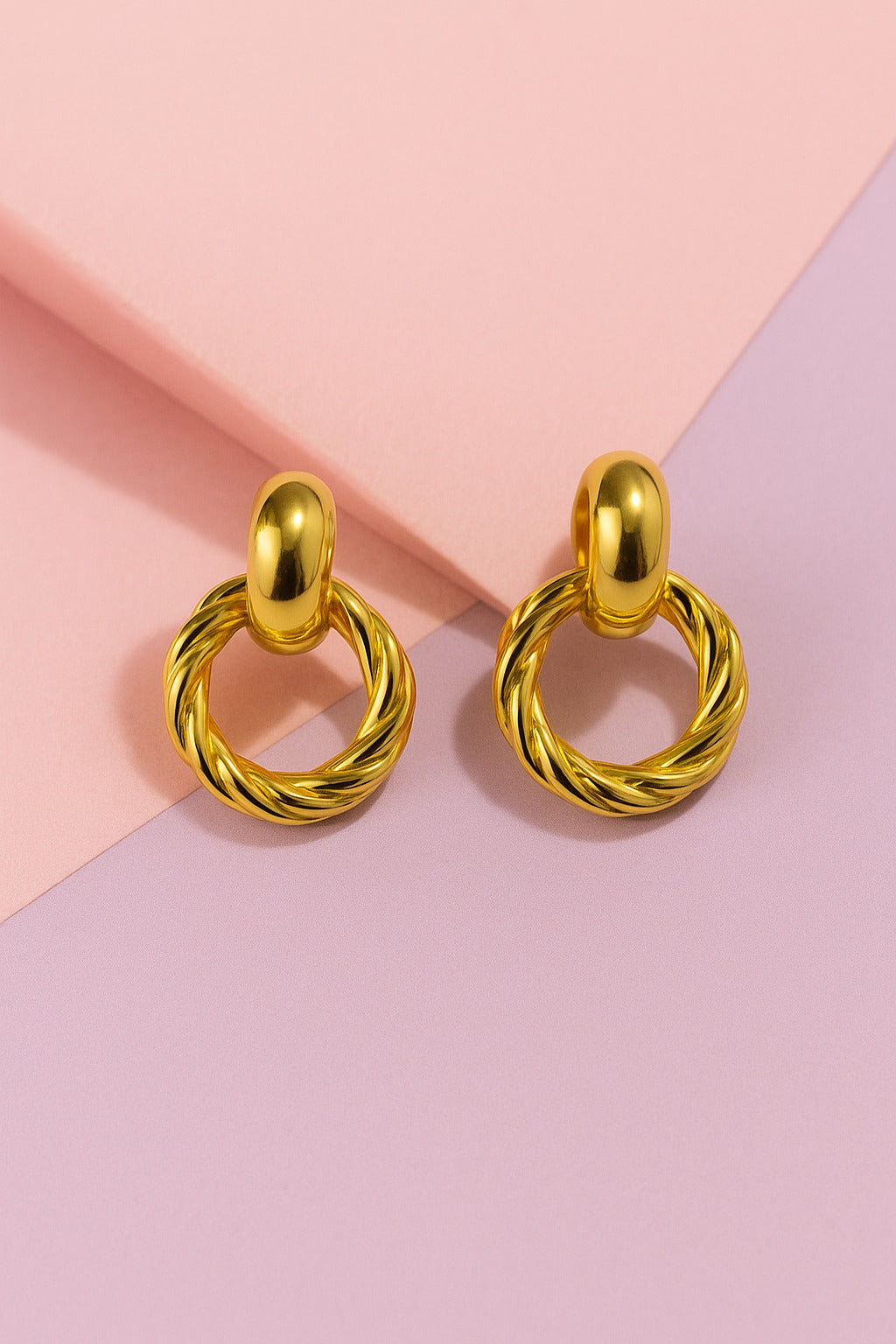 Gold hoop earrings on a pink and beige background