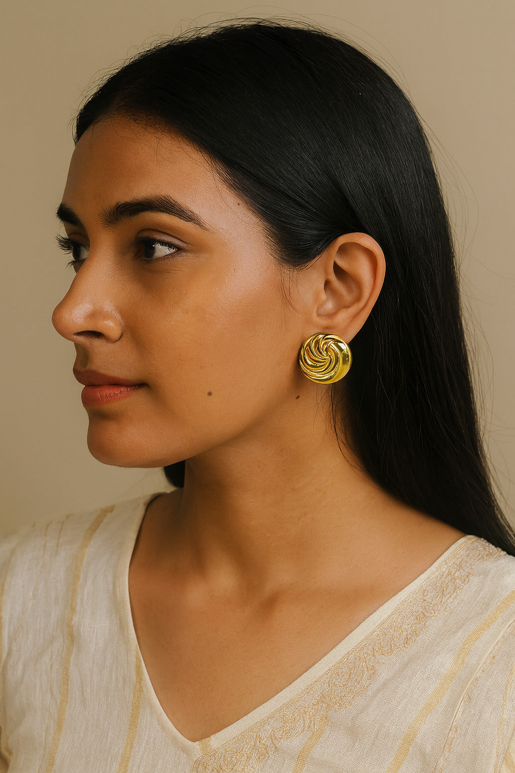 Woman wearing gold earrings with a neutral background