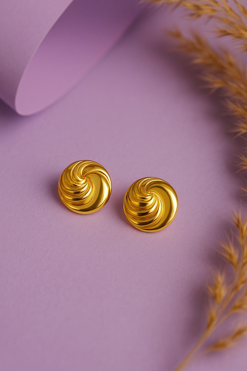 Gold spiral earrings on a purple background with dried grass