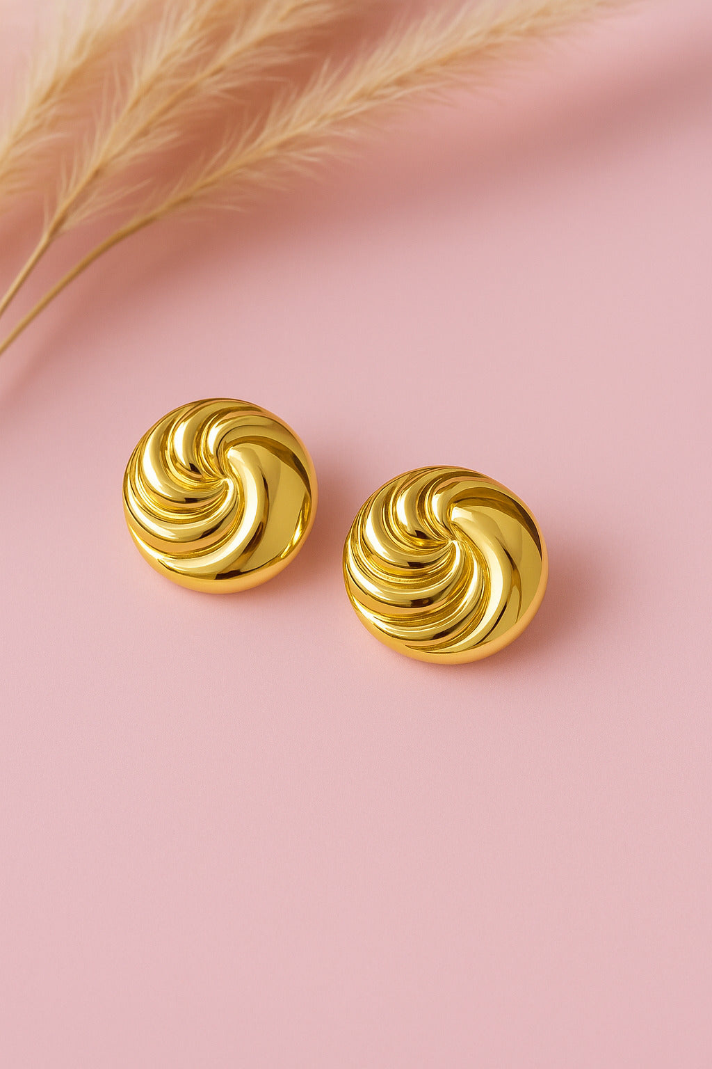 Gold spiral earrings on a pink background with a feather