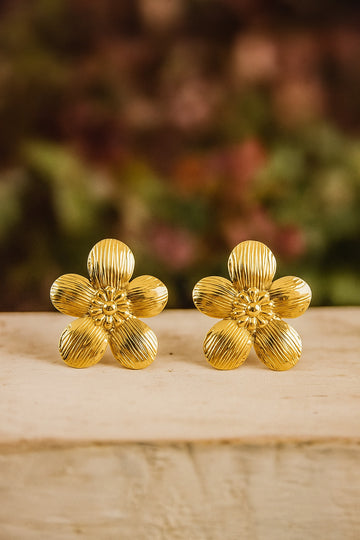 Pair of gold flower-shaped earrings on a wooden surface with a blurred natural background