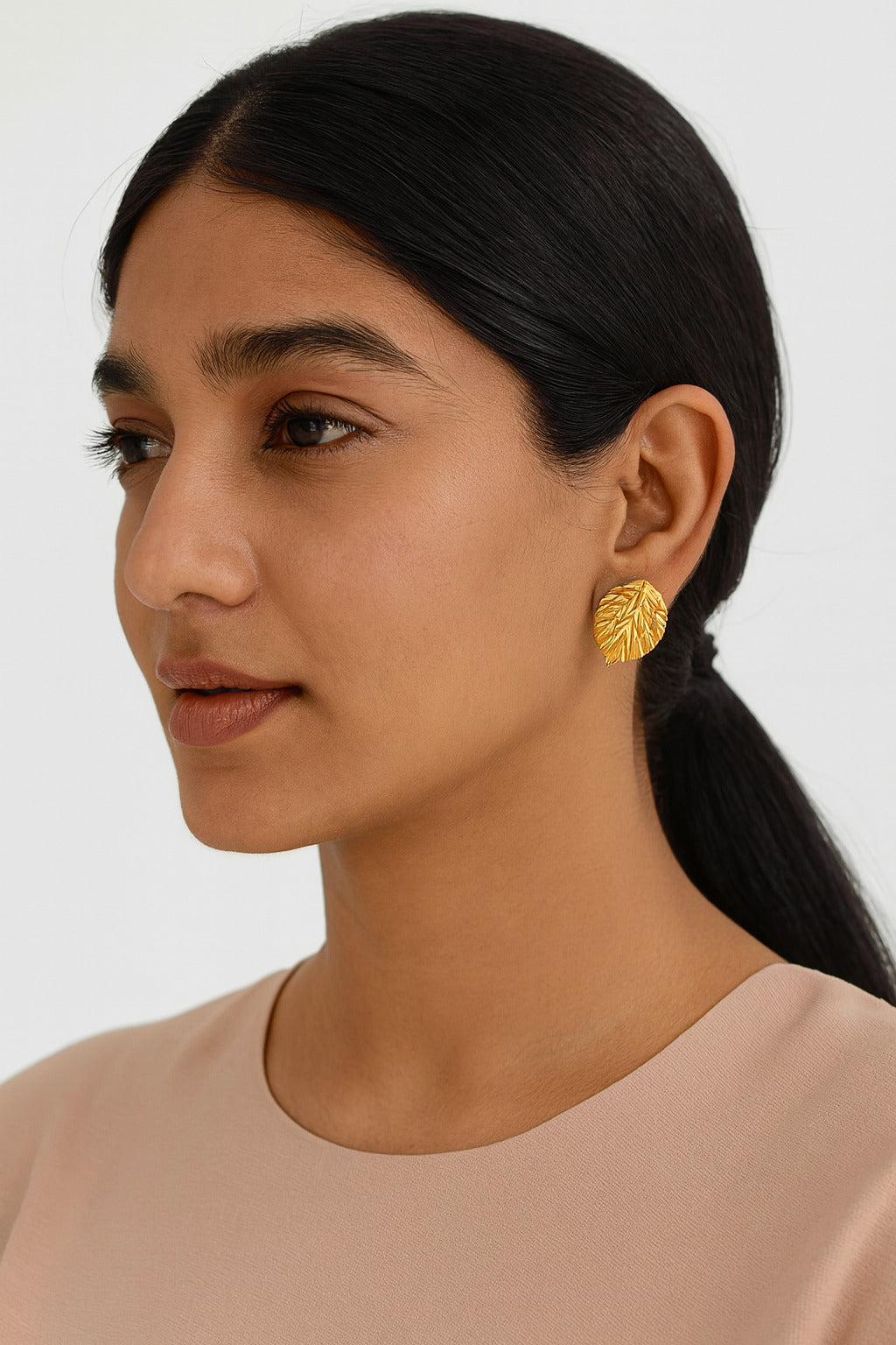 Woman wearing gold leaf earrings against a neutral background