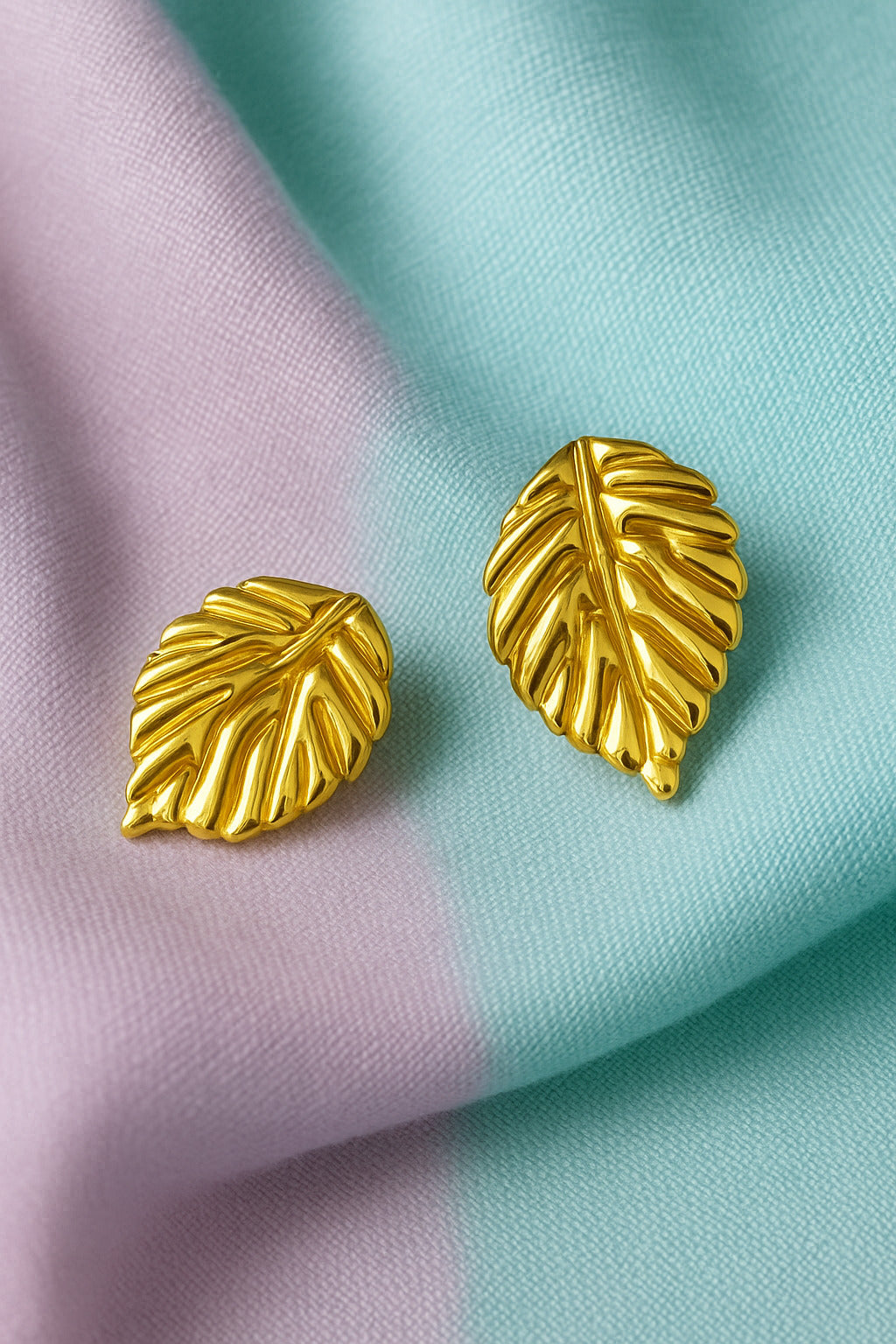 Gold leaf-shaped earrings on a colorful fabric background