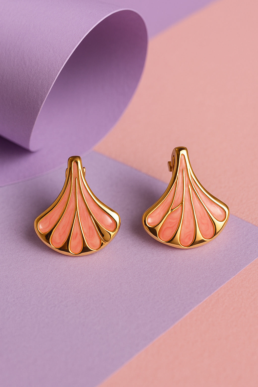 Pair of gold and pink earrings on a two-tone purple and pink background