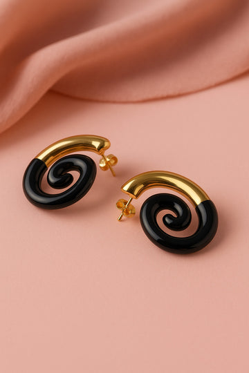 Black spiral earrings with gold accents on a pink fabric background