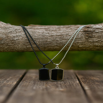 Two black dog tag necklaces on a wooden surface with a natural background