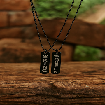 Two black metal pendants with 'KING' and 'QUEEN' on a wooden surface.