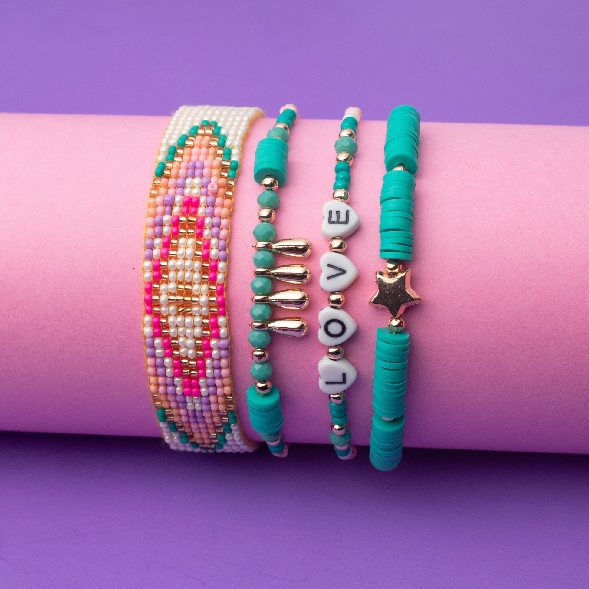 Set of colorful beaded bracelets on a pink roll with a purple background