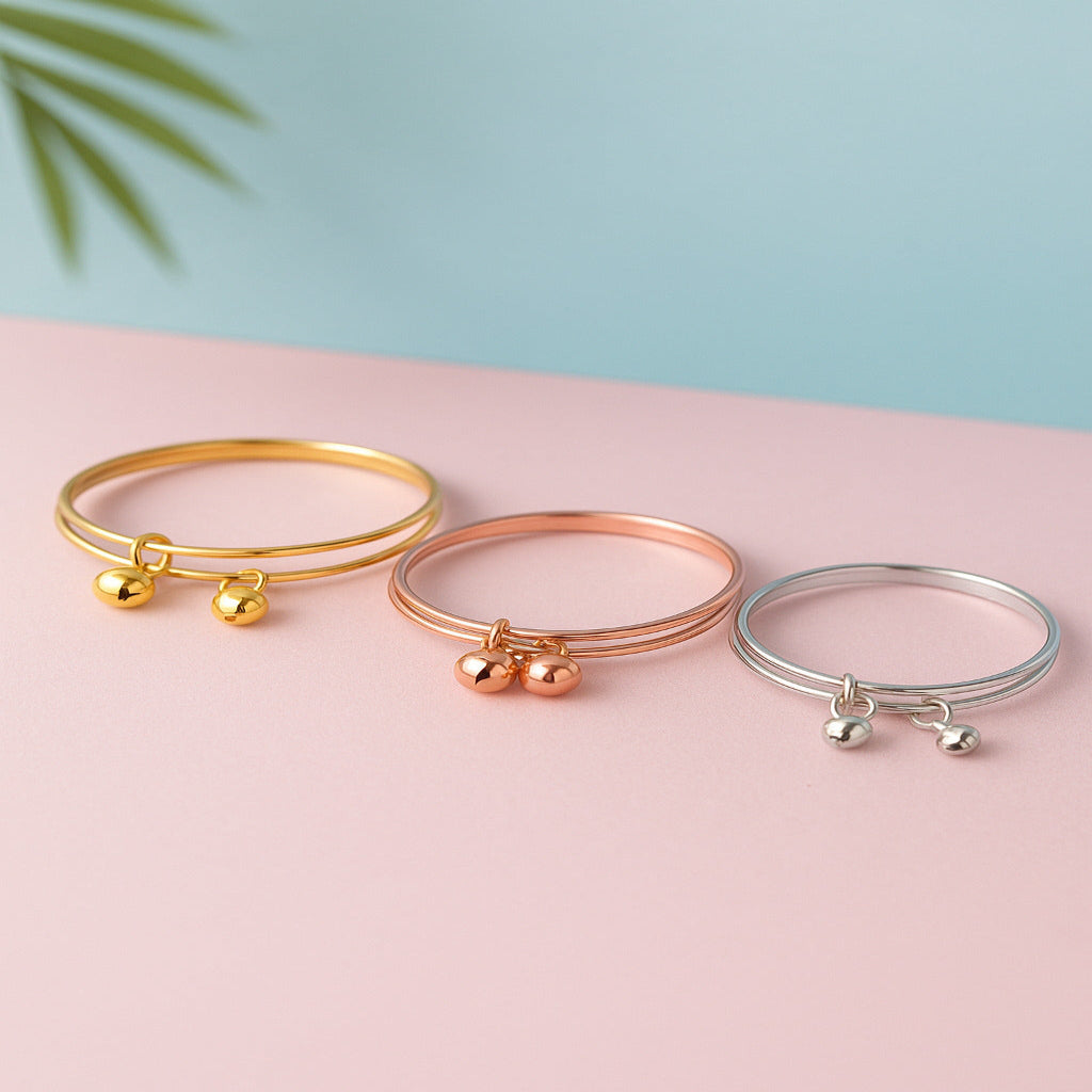 Three bangle bracelets in gold, rose gold, and silver on a pink surface with a light blue background.