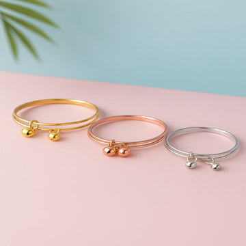 Three bangle bracelets in gold, rose gold, and silver on a pink surface with a light blue background.