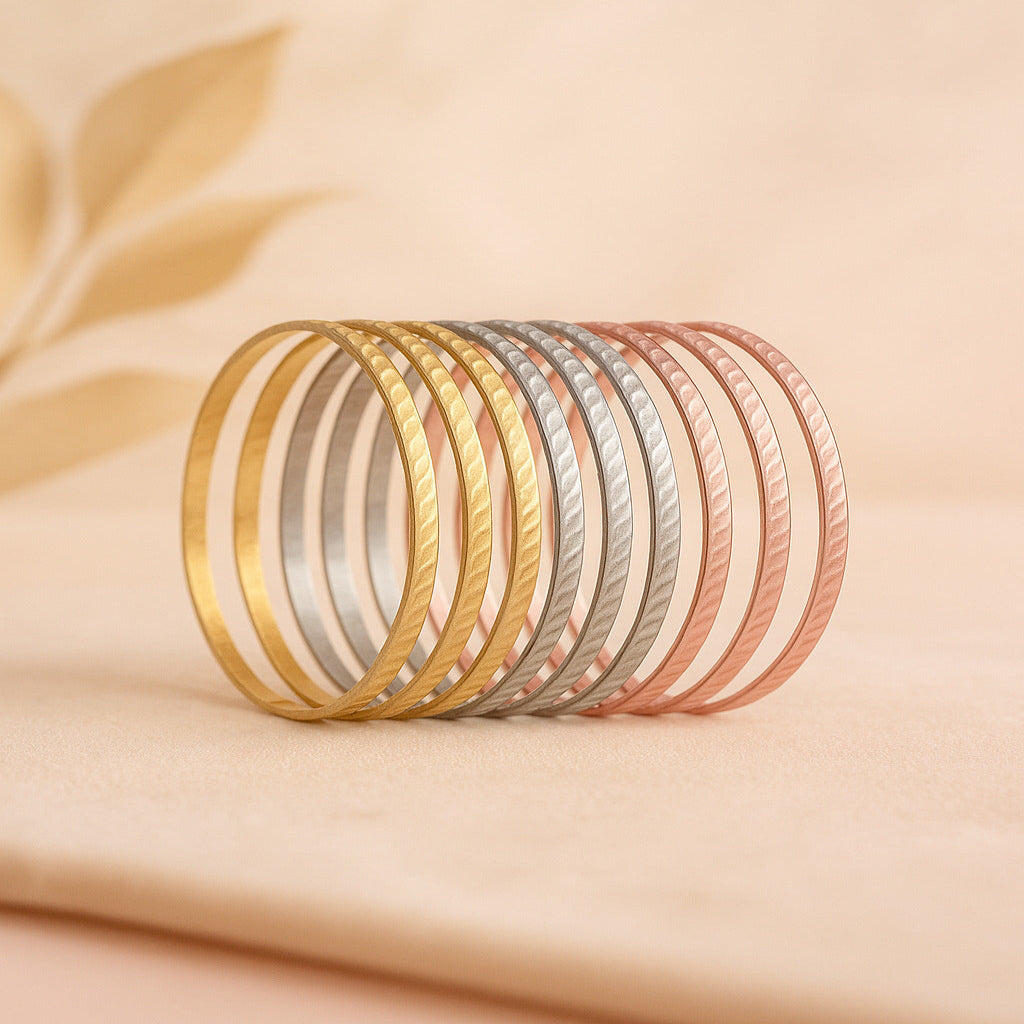 Set of gold, silver, and rose gold bangles on a beige fabric background