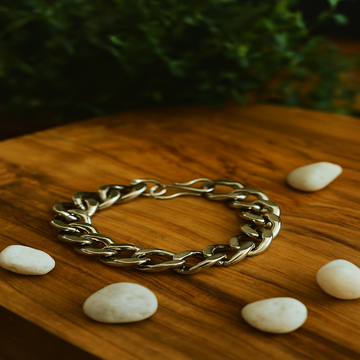 Gold chain bracelet on a wooden surface with stones and blurred greenery